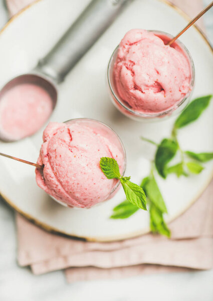 Healthy low calorie summer dessert. Homemade strawberry yogurt ice cream with fresh mint in glasses on plate over grey marble table background, top view, close-up. Clean eating, dieting food concept