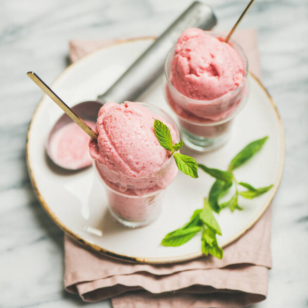Healthy low calorie summer dessert. Homemade strawberry yogurt ice cream with fresh mint in glasses over light grey marble table background, square crop. Clean eating, dieting food concept