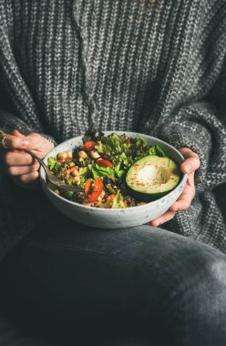 Sağlıklı vejetaryen yemeği. Kadın gri kot pantolon ve sıcak kazak taze salata, avokado, tahıl, fasulye, bir kase tutarak kavrulmuş sebze. Temiz yemek, vegan diyet gıda kavramı, superfood,