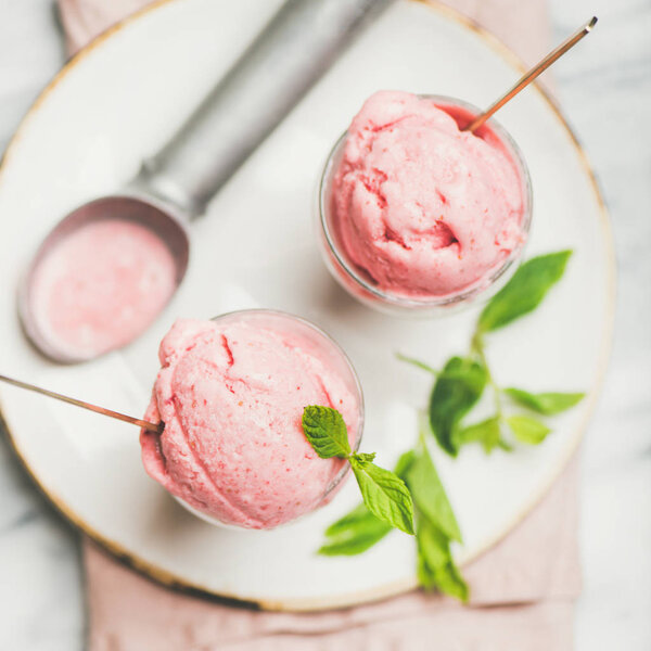 Healthy low calorie summer dessert. Homemade strawberry yogurt ice cream with fresh mint in glasses over light grey marble table background, top view, square crop. Clean eating, dieting food concept