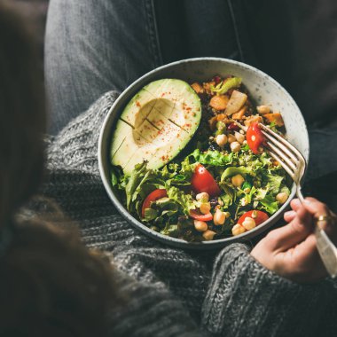 Sağlıklı vejetaryen yemeği. Kot pantolon ve yün kazak holding kase taze salata, avokado yarım, tahıl, fasulye, kavrulmuş sebze, üstten görünüm, kadında kare kırpma. Superfood, gıda kavramı yeme temiz