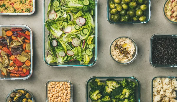 Healthy vegan dishes in containers. Flat-lay of fresh and cooked vegetable salad, legumes, beans, olives, sprouts, hummus dip, couscous for take-away lunch, top view. Spring menu, dieting food concept