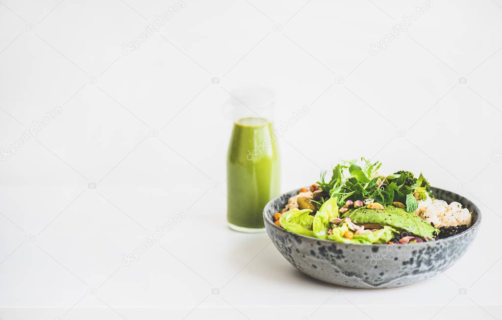 Healthy dinner or lunch at home. Vegan superbowl or Buddha bowl with hummus, vegetable, fresh salad, beans, couscous and avocado and green smoothie in bottle over white background, copy space