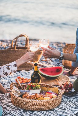 Gün batımında yaz plaj pikniği. Taze meyve ve lezzetli meze tepsiile deniz kenarında hafta sonu piknik açık havada olan genç çift, köpüklü şarap ile gözlük klinking