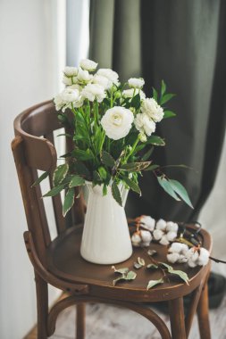 Arkasında beyaz duvar ve perde ile ahşap vintage sandalyede emaye sürahi Bahar beyaz buttercup çiçekler. Düğün buketi, çiçekçi dükkanı, Kadınlar Günü tatil veya bahar ruh kavramı