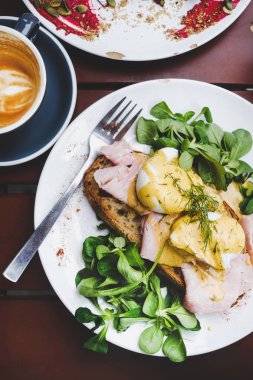 Trendy kahvaltı seti. Kafe masada yeşil salata ve domuz jambonu ile ekşi hamur ekmek tost üzerinde haşlanmış Yumurta Benedict Flat-lay, üst görünümü