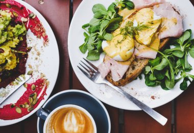 Trendy kahvaltı seti. Yeşil salata ve domuz jambonu ve kafe masada kahve fincan ıhlamalı yumurta Benedict düz yatıyordu ekşi hamur ekmek tost, üst görünümü