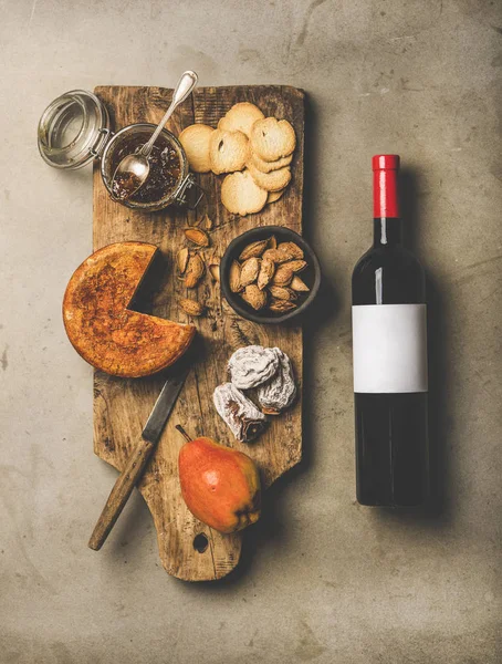 Wine and snack set. Flat-lay of wine bottle with blank label, vintage corkscrews, cheese and appetizers board over concrete background, top view. Party food concept