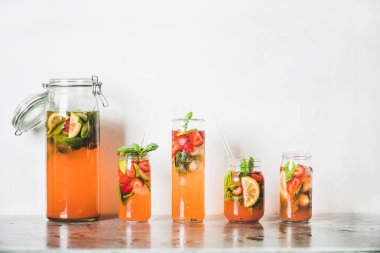 Ev yapımı çilek ve fesleğen limonata veya gri beton masa üzerinde çevre dostu plastik içermeyen pipetler ile cam bardak buzlu çay, arka planda beyaz duvar, kopya alanı. Soğuk ferahlatıcı meşrubat
