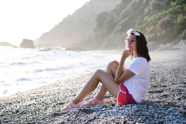 모양과 선글라스의 아름다운 여성은 꿈꾸고 지중해의 조약돌 해변에서 휴식을 취하고 — 스톡 사진