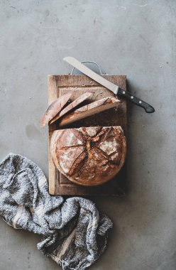 Flat-lay of freshly baked sourdough wholegrain bread loaf on rustic wooden board over grey concrete table background, top view clipart
