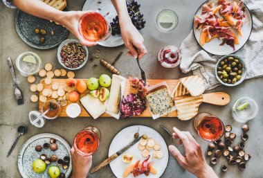 Yaz ortası şarap ve atıştırmalıklarla piknik. Charcuterie ve peynir kurulu, gül şarabı, fındık, zeytin ve halkların elleri şarap kadehleri tutan ve beton masa arka plan üzerinde kutluyor Flat-lay, üst görünümü