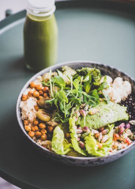 Sağlıklı akşam yemeği veya evde öğle yemeği. Vegan superbowl veya buda kase humus, sebze, taze salata, fasulye, kuskus ve avokado ve şişe içinde yeşil yüzlü masada