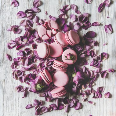 Düz-tatlı pembe makarna kurabiye yığını ve ahşap arka plan, üst görünüm, kare kırpma üzerinde gül tomurcukları ve yaprakları yatıyordu. Gıda dokusu, arka plan ve duvar kağıdı