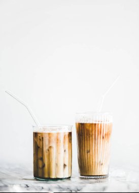 Mermer masada pipetler ile gözlük ev yapımı buzlu latte kahve, arka planda beyaz duvar, kopya alanı. Yaz soğuk serinletici içecek kavramı