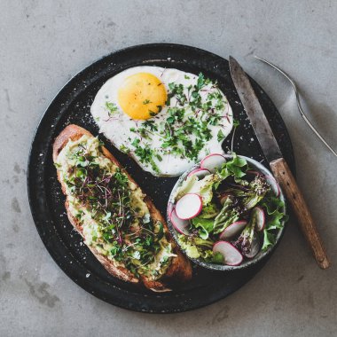 Sağlıklı kahvaltı. Otlar ve lahana ile ekşi hamur ekmek üzerinde avokado tost Düz yatıyordu, gri beton arka plan üzerinde kişniş ve salata ile kızarmış yumurta, üst görünümü, kare ürün. Temiz yeme konsepti