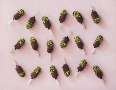 Dondurma lı buzlu şeker deseni. Pastel pembe arka plan üzerinde antep fıstığı krema ile çikolata sırlı dondurma pops Düz yatıyordu, üst görünümü. Yaz soğuk tatlı sağlıklı vegan tatlı