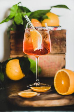 Aperol Spritz aperatif turuncu ve buz küpleri ile cam beton masa üzerinde çevre dostu cam saman, arka planda beyaz duvar, seçici odak, yakın çekim. Yaz serinletici içecek konsepti