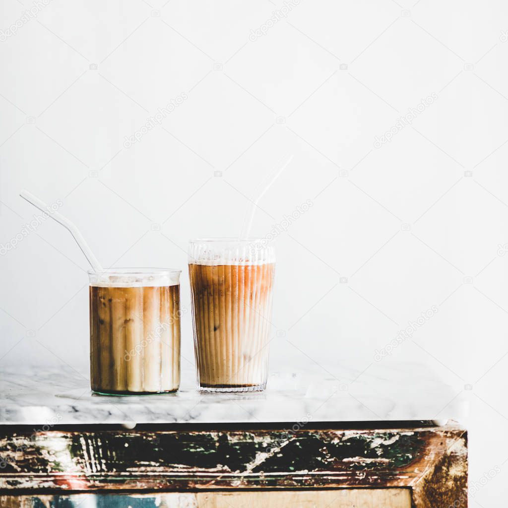 Homemade iced latte coffee in glasses with straws on grey marble table, white wall at background, copy space, square crop. Summer cold refreshing drink concept