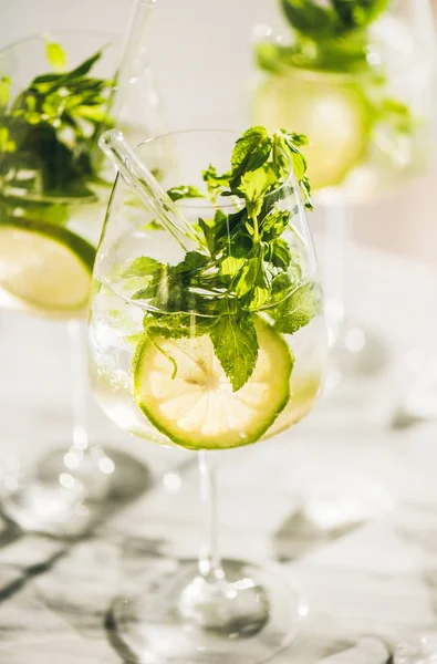 Hugo Köpüklü şarap kokteyli taze nane yaprakları ve beyaz mermer mutfak tezgahı, seçici odak üzerinde çevre dostu pipetler ile gözlük kireç dilimleri ile. Soğuk serinletici yaz alkollü içecek