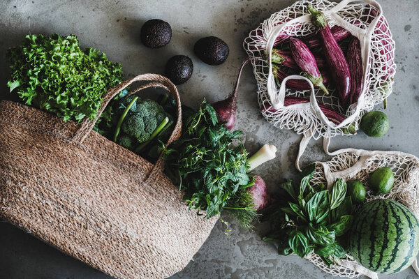Flat-lay of of grocery jute and net bags full of fresh vegetables, greens, fruit from local farmers market over grey concrete background. Zero waste, healthy, eco-friendly, vegan, clean eating concept