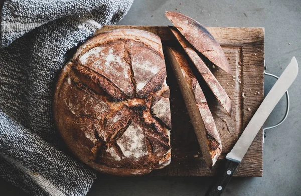 在灰色混凝土桌子背景的质朴木板上 平铺新鲜出炉的酸面包面包和面包片 顶视图 — 图库照片