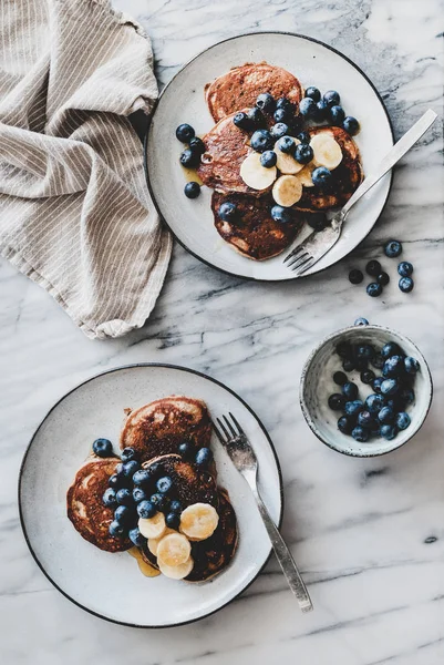 Healthy comfort breakfast set. Flat-lay of banana pancakes with fresh blueberry and honey over white marble table background, top view