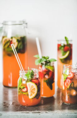 Ev yapımı çilek ve fesleğenli limonata ya da cam bardaklarda buzlu çay gri beton masa üzerinde çevre dostu plastik pipetler, arka planda beyaz duvar, seçici odaklanma. Soğuk, ferahlatıcı bir içecek.