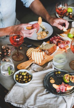 Yaz ortasında şarap ve atıştırmalıklarla piknik. Şarküteri ve peynir tahtası, gül şarabı, fındık, zeytin, taze meyve ve erkek eli.
