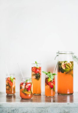 Soğuk, ferahlatıcı bir içecek. Ev yapımı taze çilek ve fesleğenli limonata veya cam bardaklarda buzlu çay gri beton masa üzerinde çevre dostu plastik pipetler, arka planda beyaz duvar, kopyalama alanı.