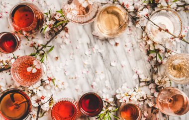 Gül şarabının gölgeleri. Farklı renklerde gül şarabı ve beyaz arka planda bahar çiçeği, üst manzara, kopyalama alanı. Şarap dükkanı, bar, tatma, şarap listesi konsepti.