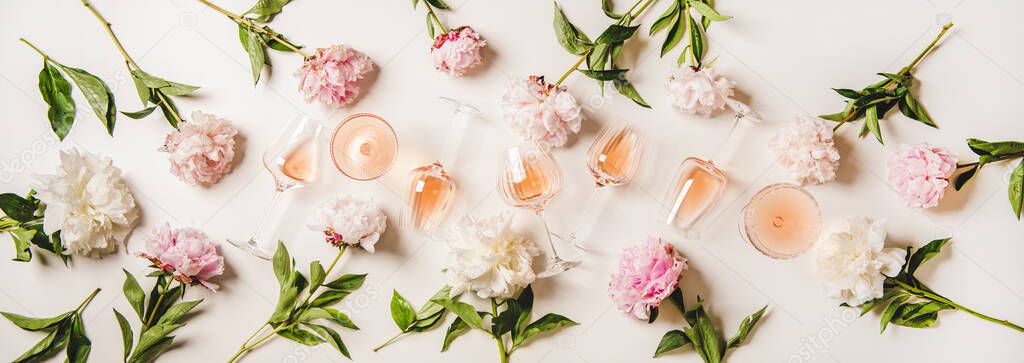 Rose wine variety layout. Flat-lay of rose wine in various glasses and summer blooming peony flowers over white background, top view. Summer drink for party, wine shop or wine tasting concept
