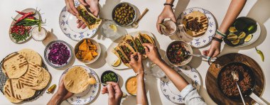 Meksika Taco yemeği yiyen arkadaşlar. Sığır etli taco, domates salsası, tortilla, bira, nachos ve insanlar beyaz masa, üst manzara. Meksika mutfağı, toplanma, ziyafet, konfor yiyecek konsepti