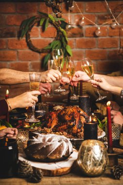 Noel 'i ya da yeni yılı kutlayan aile. Halkın elleri şampanya kadehleriyle tezahürat yapıyor. Kavrulmuş hindi, çikolatalı pasta, mumlar, arka planda kırmızı tuğla duvar.