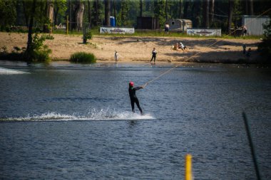 Adam yazın kask ve dalgıç kıyafetiyle suda wakeboard yapıyor..
