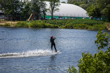 Adam yazın kask ve dalgıç kıyafetiyle suda wakeboard yapıyor..