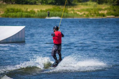 Adam yazın kask ve dalgıç kıyafetiyle suda wakeboard yapıyor..