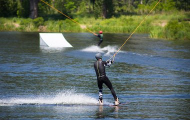 Adam yazın kask ve dalgıç kıyafetiyle suda wakeboard yapıyor..