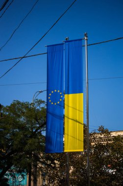 Avrupa Birliği bayrağı ve Ukrayna bayrağı mavi gökyüzü arka planında dalgalanıyor