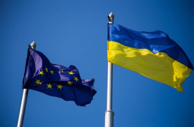 Avrupa Birliği bayrağı ve Ukrayna bayrağı mavi gökyüzü arka planında dalgalanıyor