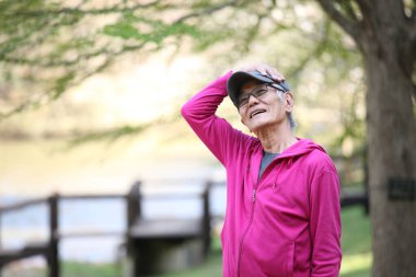 Pembe parka giyen yaşlı bir Japon açık havada boyun esnetiyor.