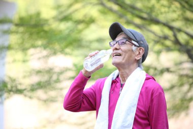 Yaşlı Japon adam, egzersizden sonra terli ve susuz halde dışarıda su içiyor.