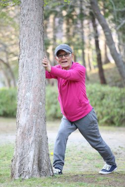 Pembe parka giyen yaşlı Japon adam ağaçtan buzağıyı geriyor.