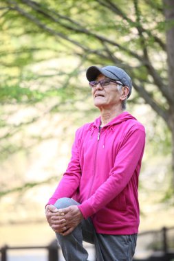 Pembe giysili yaşlı Japon adam diz boyu göğüs gererek ayakta duruyor.