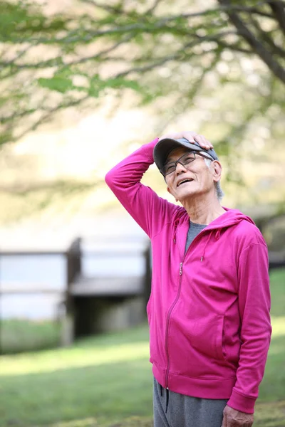 Pembe giysili yaşlı Japon adam dışarıda boyun esnetiyor.