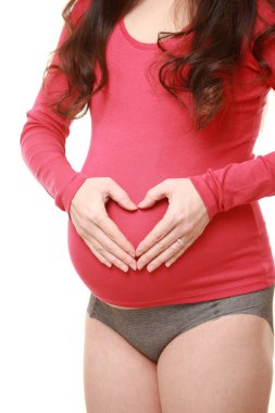 Hamile kadın elleriyle kalp yapıyor.