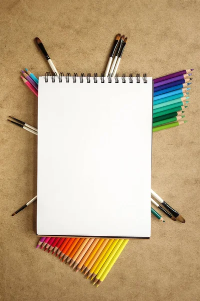 Rainbow of colour pencils. Gradation of colors in a line. Painting & School Supplies. Copy space. Notepad in center
