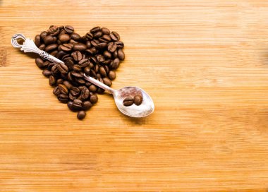 Ahşap masada gümüş kaşık kahve fasulye kalp ile delinmiş