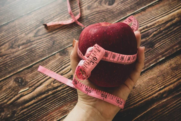 Weight loss and diet. Big juicy red apple and a tape for measuring the body. Hand holding it. Proper nutrition and fitness. Flat lay on a wooden table