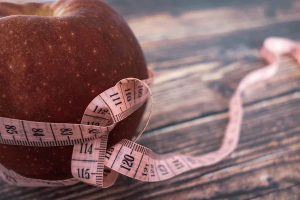 Weight loss and diet. Big juicy red apple and a tape for measuring the body. Proper nutrition and fitness. Flat lay on a wooden table. Macro